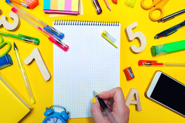 the student makes notes in a notebook. copy space. school accessories on a desk on a yellow background. concept of education. stationery. watches, colored pens, phone, markers.