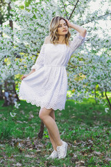 Naklejka na ściany i meble Beautiful blonde girl with blond hair in a dress on a background of spring blooming trees