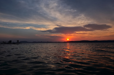 sunset over lake Balaton, angling men silhouette - golden bridge, calm water, close up, hills in background
