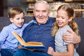 Waist up of cheerful elderly man reading for his grandchildren