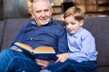 Pleasant little boy reading a book with his grandfather