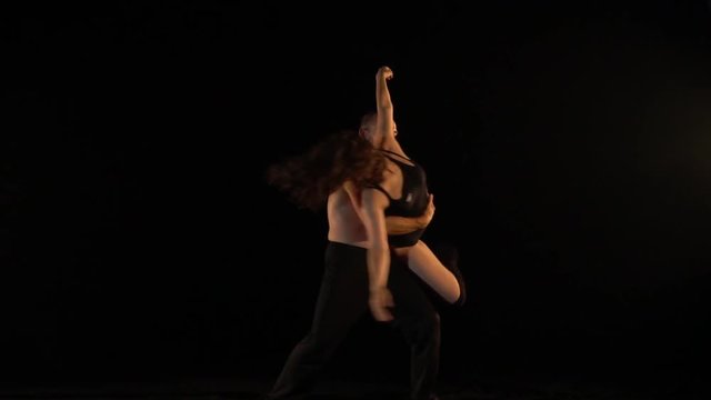 man and woman together perform acrobatics tricks on a black background, slow
