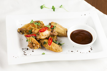 Grilled baked chicken wings with chili pepper and hot sauce on white plate