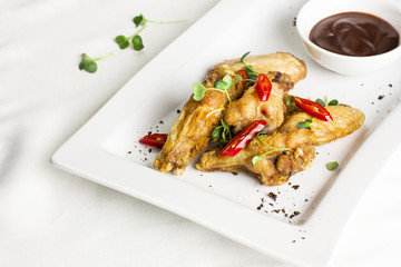 Grilled baked chicken wings with chili pepper and hot sauce on white plate