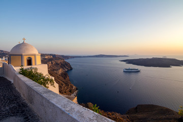 Fototapeta na wymiar Elevated romantic sunset scene on Santorini. Fira, Greece, from above. Amazing golden hour view from public path walk towards volcano in the caldera. Shortly before the sunset, church in the image