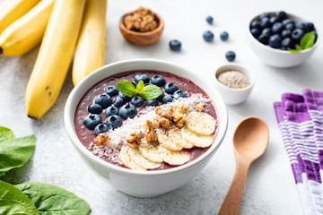 Acai smoothie bowl topped with banana, chia seed, blueberries, walnuts and coconut on concrete background