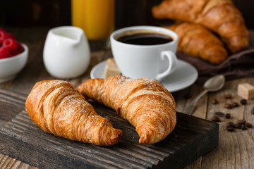 Breakfast with croissants, coffee, orange juice and berries on wood background