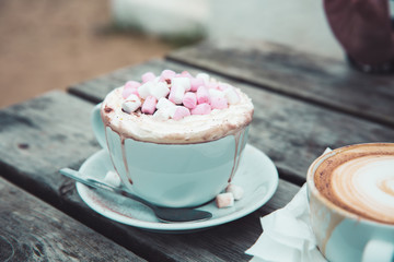 A luxury hot chocolate drink in a posh cup and saucer with whipped cream and marshmallows melting on top