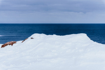 High red rocks rise above the snow-covered coast of the sea in winter in spooky cold and strong...