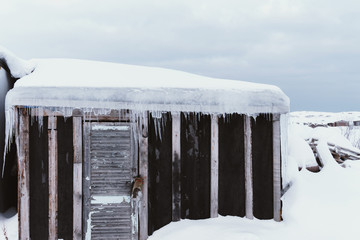 Old dilapidated and partially destroyed houses in which people still live in the village in the far north in winter under the thick slime of white snow