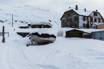 Old dilapidated and partially destroyed houses in which people still live in the village in the far north in winter under the thick slime of white snow