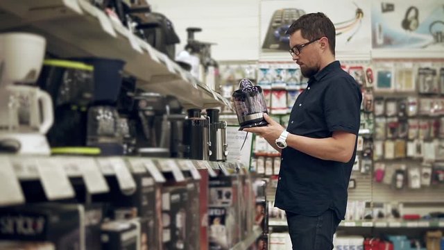 Grown man holding electric juicer in a appliance store. Man wants to purchase juicer for home. Squeezing fresh juice in summer.