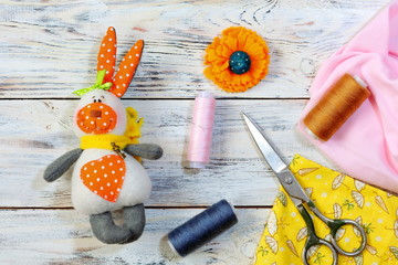 Top view of on a textile bunny toy, cloth scraps, thread reels and scissors. Colorful threads and...