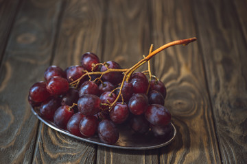 close-up shot of branch of fresh grapes on vintage metal plate on rustic wooden table