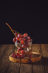 close-up shot of ripe grapes in vintage metal bowl on rustic wooden table on black