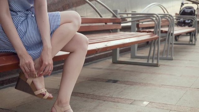 Young woman fastens sandals sitting on the bench.