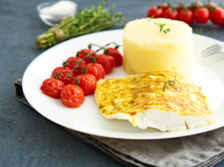 Fish cod baked in oven with mashed potatoes, tomatoes, diet healthy food. Dark gray background, side view