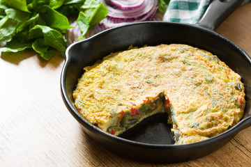 Frittata made of eggs and vegetables in a iron pan, on wooden table.