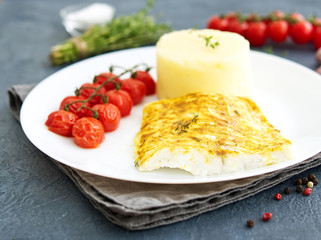 Fish cod baked in oven with mashed potatoes, tomatoes, diet healthy food. Dark gray background, side view