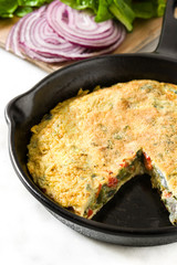 Frittata made of eggs and vegetables in a iron pan, on white marble