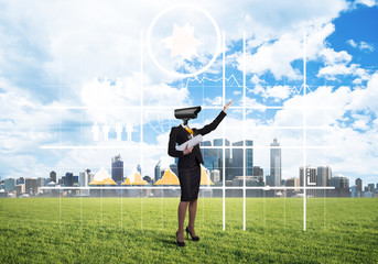 Camera headed woman standing on green grass against modern cityscape