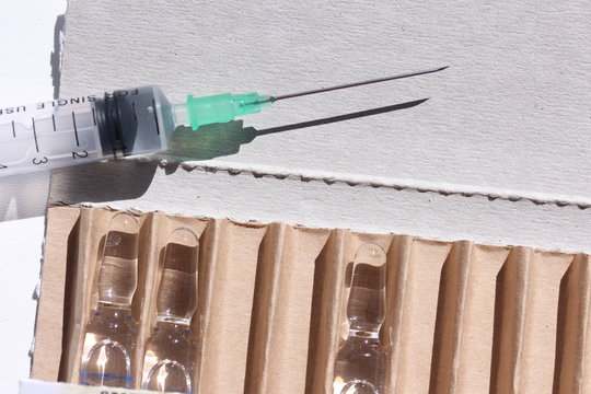 Novocaine in ampoule in the box and syringe on the table.

