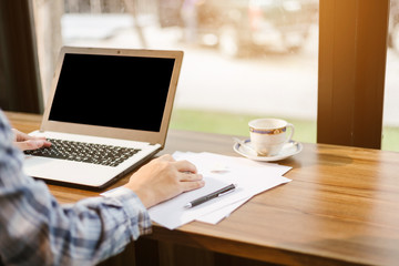 Close-up of businessman working with laptop with blank black screen,smart phone and document on in coffee shop like the background.