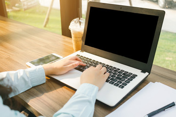 Close-up of business female working with laptop with blank black screen make a note document and smartphone in coffee shop like the background.