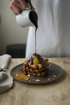 Woman pouring chocolate sauce on waffles
