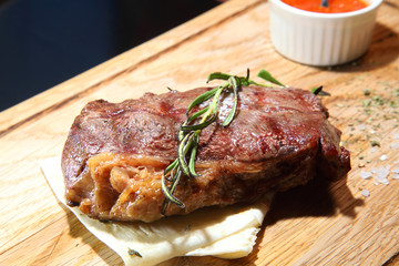 Steak medium roast on a wooden board with sauce and salt.