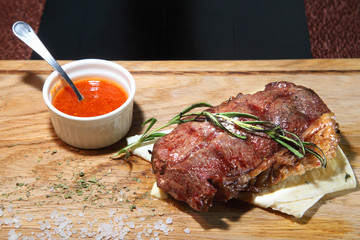Steak medium roast on a wooden board with sauce and salt.