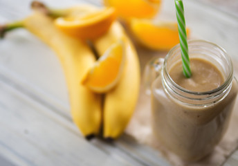 Fresh banana and orange smoothie on wooden white table