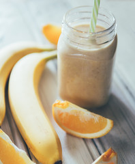 Fresh banana and orange smoothie on wooden white table