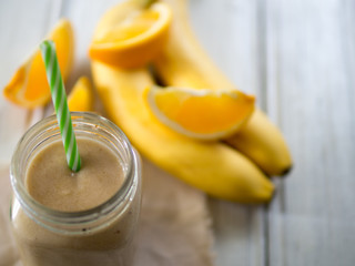 Fresh banana and orange smoothie on wooden white table