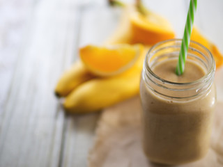 Fresh banana and orange smoothie on wooden white table