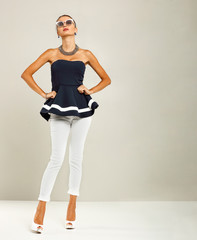 Beautiful and attractive model dressed in expensive clothes. White pants, navy blue blouse and high heels. A photo of a fashion shot in the studio.