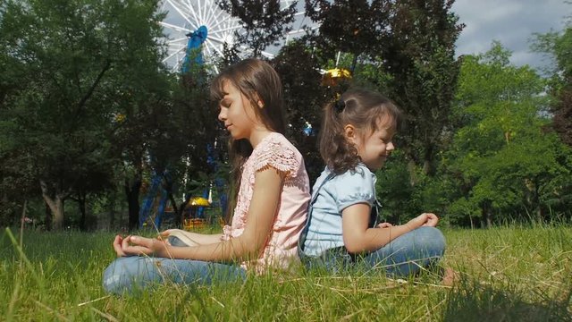 Children do yoga. Little girls meditate in the park.