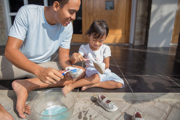  father with her toddler girl washing their shoes together 