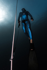 Freediver ascends from a depth along the rope holding a safety leash in a hand.