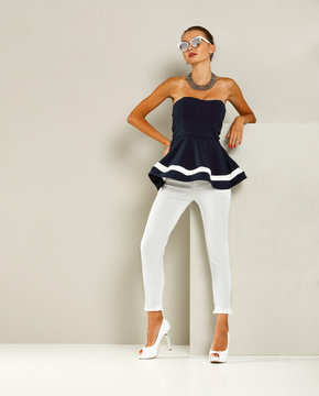 Beautiful and attractive model dressed in expensive clothes. White pants, navy blue blouse and high heels. A photo of a fashion shot in the studio.