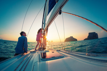 Couple of young sailors, man and woman, works with rope on the bow of the sailing boat at sunset