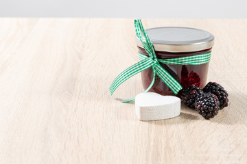 Decorated glass of homemade blackberry jam on a wooden table 
