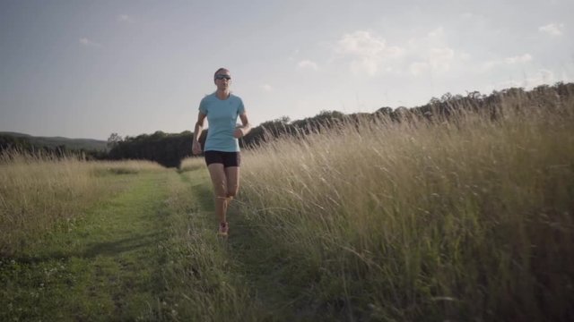 slow motion woman running on path through high dry grass

