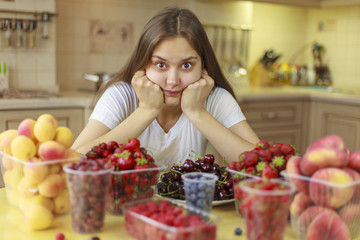 Beautiful young girl eats fruits and fresh berries in the kitchen
