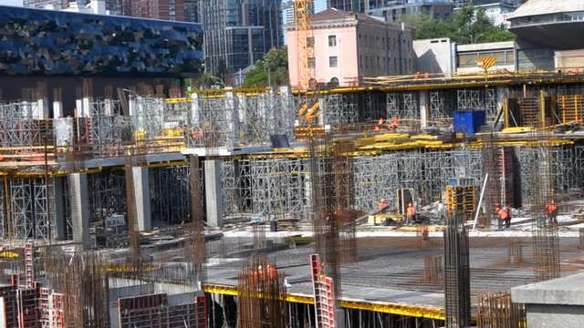 Many builder works orange protective uniform at against background of construction site high-rise buildings. Construction workers, work hard to build new building for expensive apartment and office.