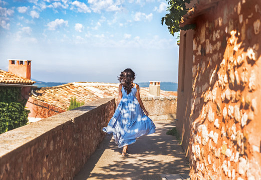 France, Provence medieval town Roussillon. French pretty young woman in blue dress with waving hair walking down the street by ancient Provencal town Roussillon. Travel and wanderlust concept.