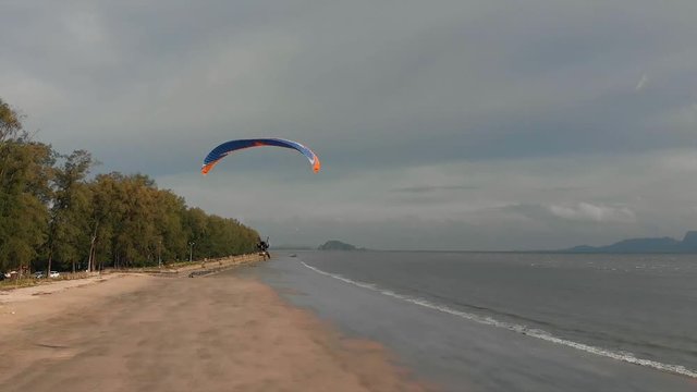 Para motor flies along the sandy beach over the sea. Background with islands view. The coast of Thailand. Trang province. Sikao. Paraglide. Paramotor.
