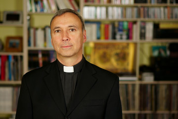 Fototapeta premium A portrait of a good looking serious catholic priest. He looks at us with interest, pensiveness, proselytising, joy, happiness, trust and peacefulness.