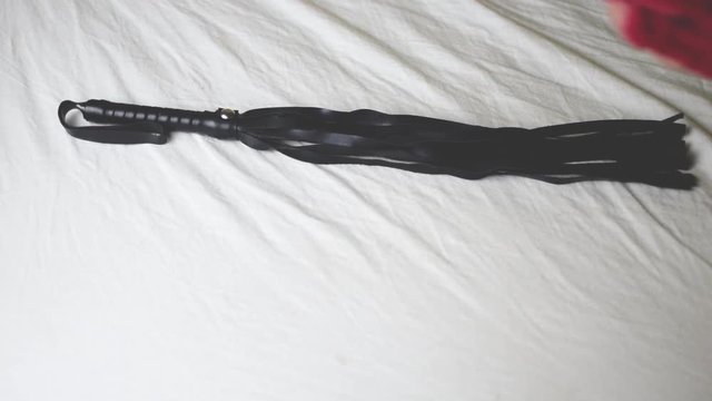 Toys for erotic games BDSM. A whip, handcuffs, clamps lie on the bed.