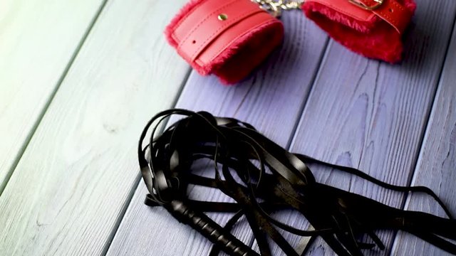Toys for erotic games BDSM. A whip, handcuffs, clamps lie on a wooden surface.
